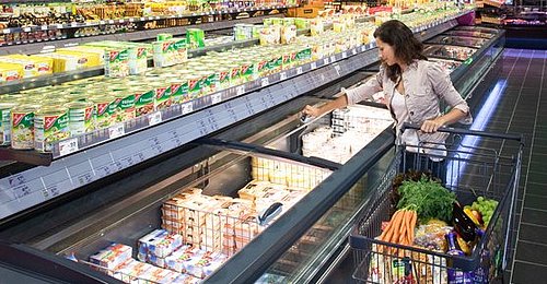 Tiefkühltruhe mit modular aufgebautem Glasschiebedeckel „EcoFlex Push Stabile“ wird von einer Dame beim Einkaufen im Supermarkt vertikal geöffnet. 